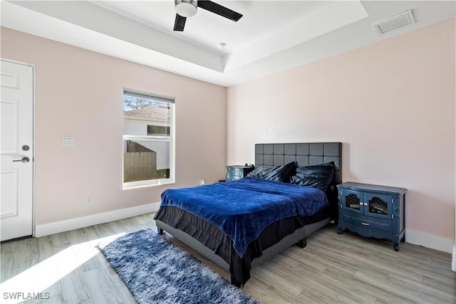 bedroom featuring a tray ceiling, ceiling fan, and light wood-type flooring