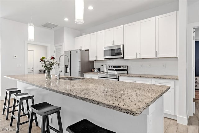 kitchen featuring sink, light hardwood / wood-style floors, pendant lighting, a kitchen island with sink, and appliances with stainless steel finishes