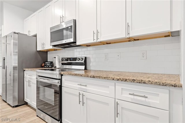 kitchen with white cabinets, appliances with stainless steel finishes, light wood-type flooring, and light stone countertops