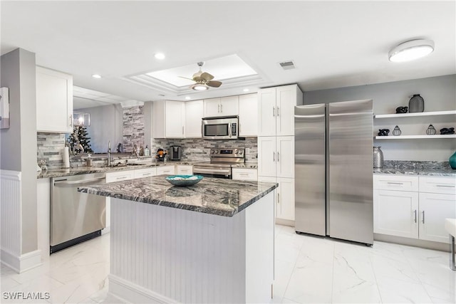 kitchen with appliances with stainless steel finishes, ceiling fan, dark stone countertops, white cabinets, and a center island