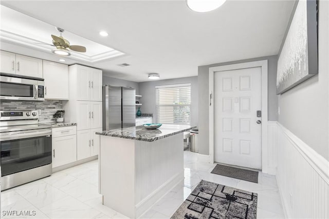 kitchen featuring ceiling fan, stainless steel appliances, a kitchen island, dark stone countertops, and white cabinets