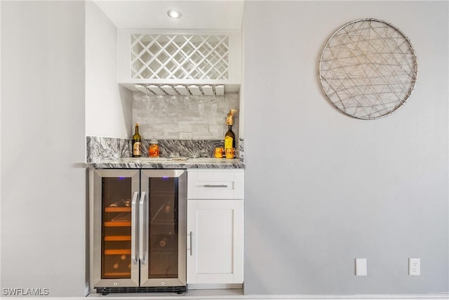 bar with tasteful backsplash, wine cooler, white cabinetry, and light stone counters