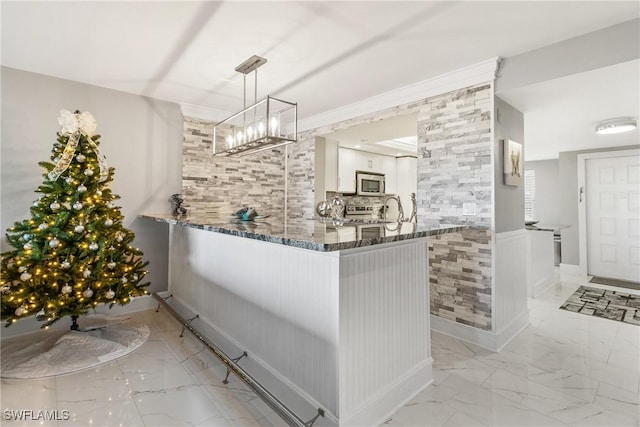 interior space with sink, dark stone countertops, appliances with stainless steel finishes, decorative light fixtures, and white cabinetry