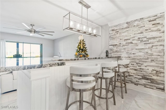 kitchen with a breakfast bar, hanging light fixtures, ceiling fan, light stone countertops, and white cabinetry