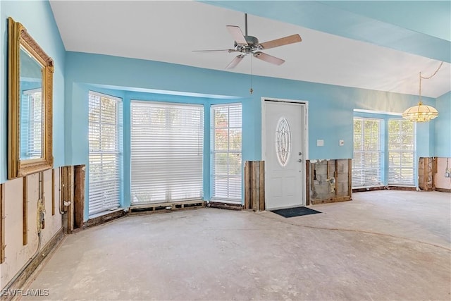 unfurnished living room with concrete flooring, ceiling fan with notable chandelier, and a wealth of natural light