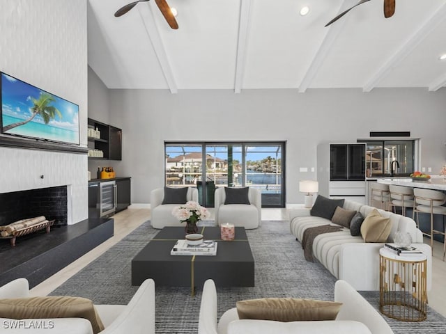 living room featuring beverage cooler, sink, high vaulted ceiling, beamed ceiling, and a fireplace