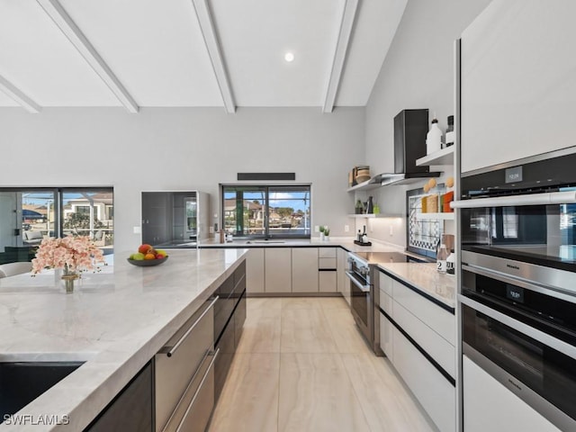 kitchen featuring a wealth of natural light, light stone countertops, beamed ceiling, and appliances with stainless steel finishes