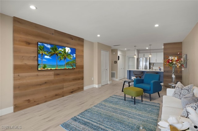 living room with light hardwood / wood-style flooring, wooden walls, and sink