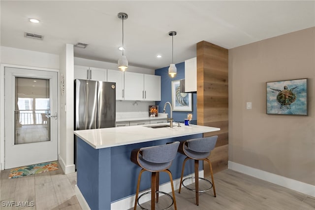 kitchen with white cabinetry, stainless steel fridge, hanging light fixtures, light hardwood / wood-style flooring, and sink