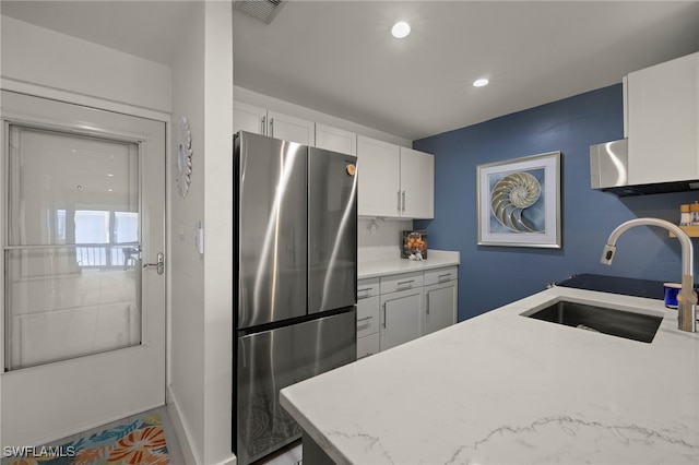 kitchen with white cabinets, stainless steel fridge, light stone counters, and sink