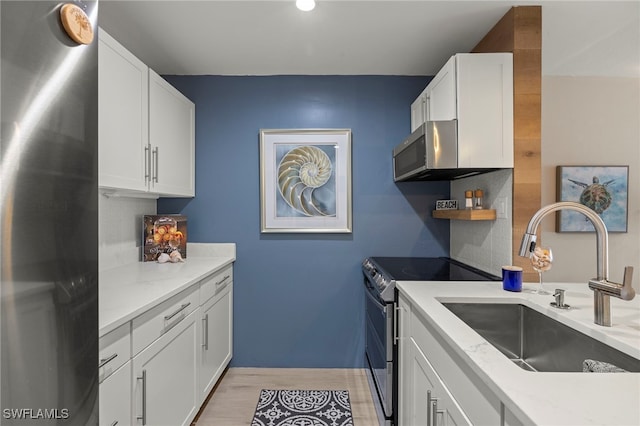 kitchen with light stone countertops, white cabinetry, stainless steel appliances, light hardwood / wood-style floors, and sink