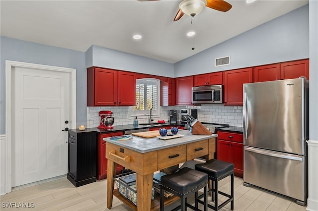 kitchen with sink, a center island, vaulted ceiling, appliances with stainless steel finishes, and ceiling fan