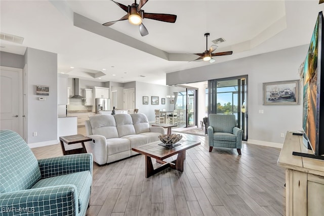 living room with ceiling fan, light hardwood / wood-style flooring, and a tray ceiling