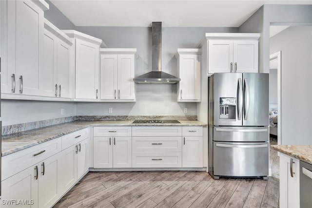 kitchen featuring white cabinets, light stone counters, wall chimney range hood, and stainless steel refrigerator with ice dispenser