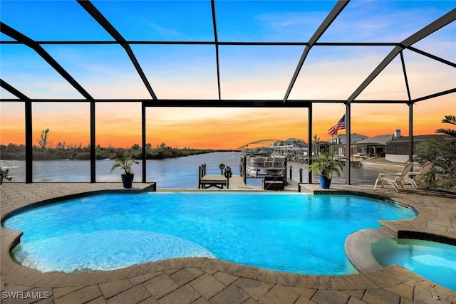 pool at dusk featuring a lanai, a water view, and an in ground hot tub