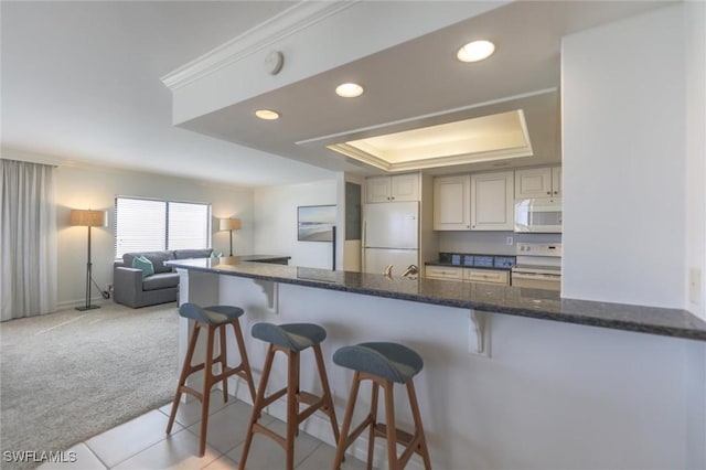 kitchen featuring white appliances, light carpet, a raised ceiling, dark stone countertops, and kitchen peninsula