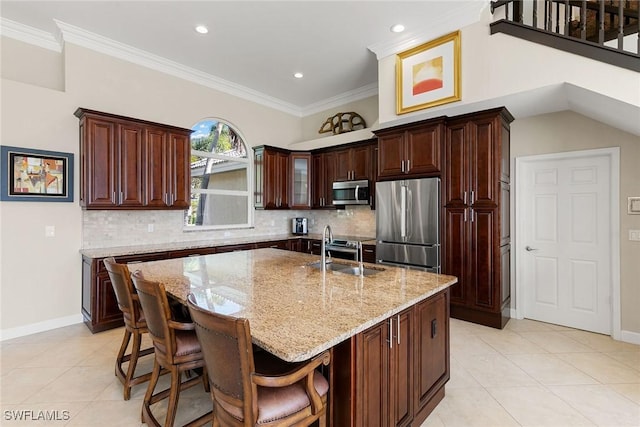 kitchen with a kitchen island with sink, sink, ornamental molding, light stone counters, and stainless steel appliances