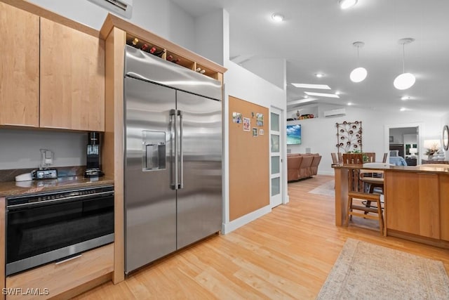 kitchen with pendant lighting, a wall mounted air conditioner, light brown cabinets, light wood-type flooring, and appliances with stainless steel finishes