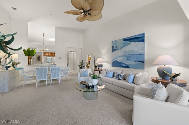 living room featuring ceiling fan, light colored carpet, and a high ceiling