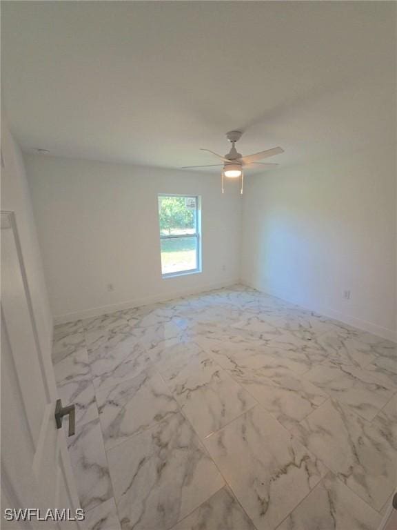 spare room featuring marble finish floor, ceiling fan, and baseboards