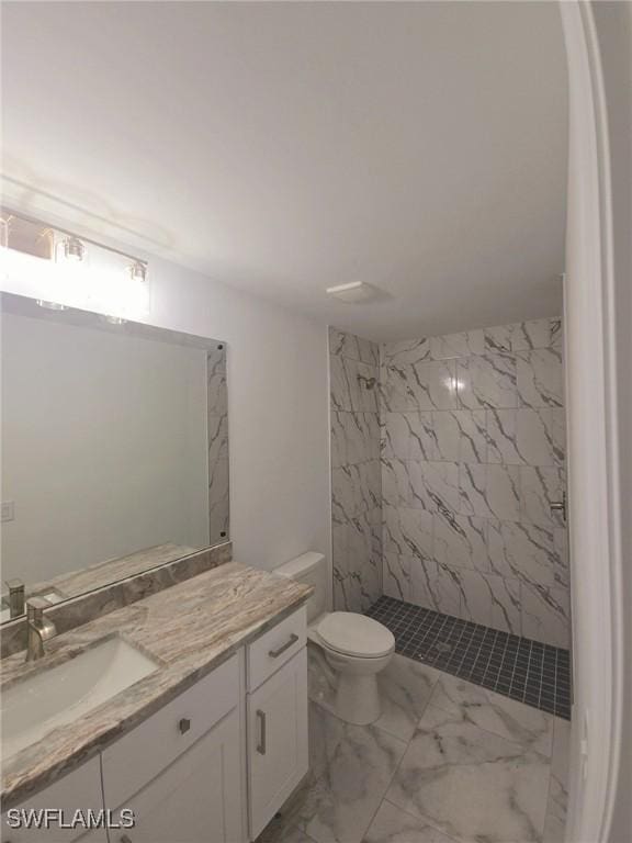 bathroom featuring vanity, a tile shower, and toilet