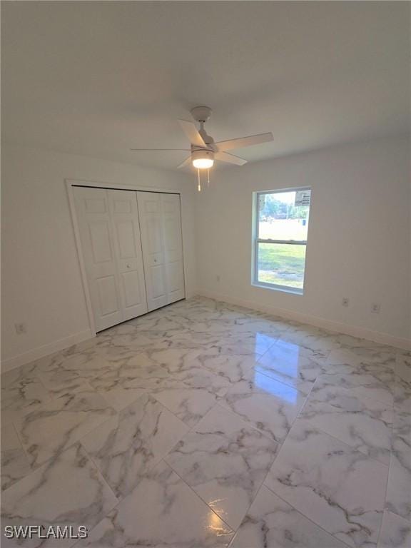 unfurnished bedroom with a closet, marble finish floor, baseboards, and a ceiling fan