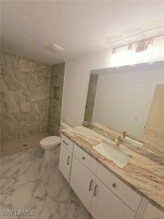 full bathroom featuring toilet, marble finish floor, a tile shower, and vanity