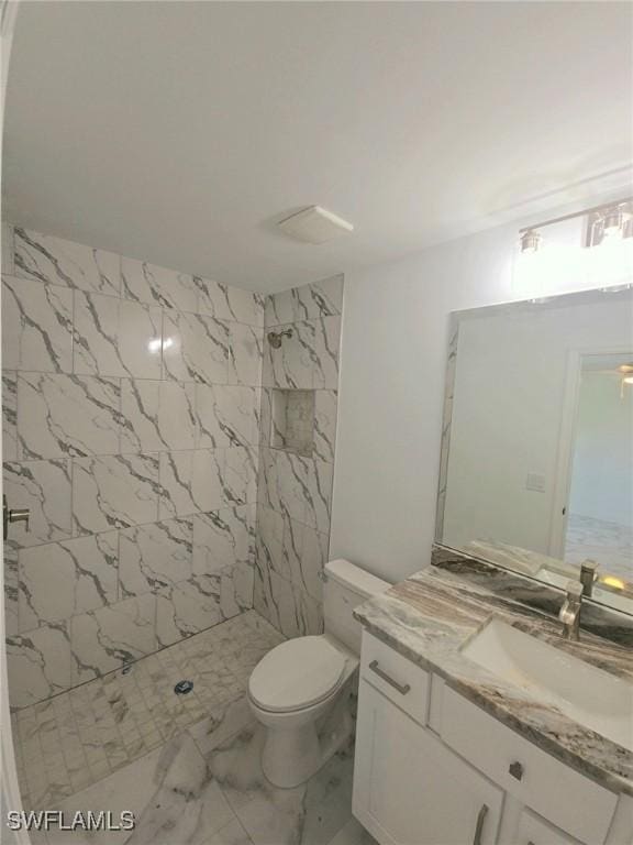 full bath with toilet, marble finish floor, tiled shower, and vanity