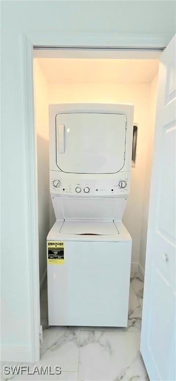 laundry area with marble finish floor, stacked washer / dryer, laundry area, and baseboards