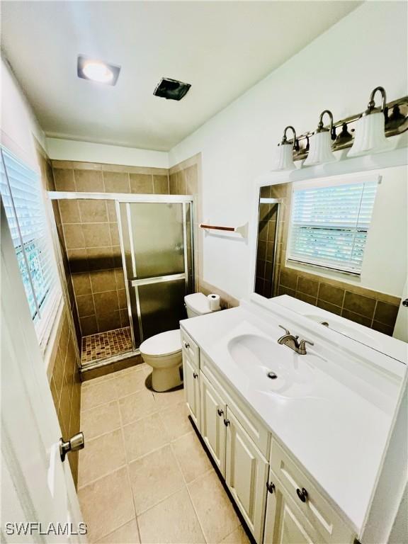 bathroom with tile patterned flooring, vanity, toilet, and a shower with shower door