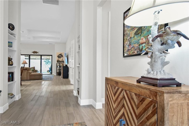 corridor featuring built in shelves, light hardwood / wood-style floors, and a raised ceiling