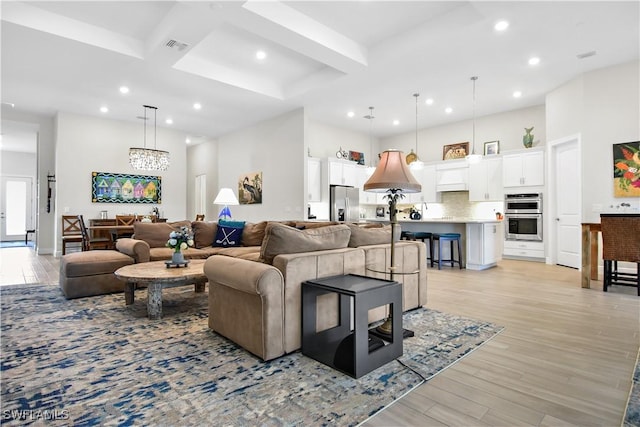 living room featuring beamed ceiling, a towering ceiling, light hardwood / wood-style flooring, and a notable chandelier