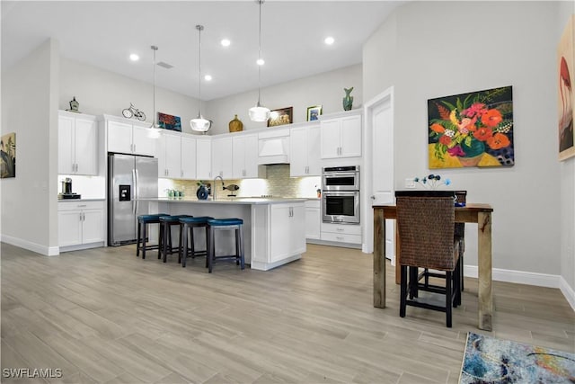 kitchen featuring white cabinets, stainless steel appliances, hanging light fixtures, and a kitchen island with sink