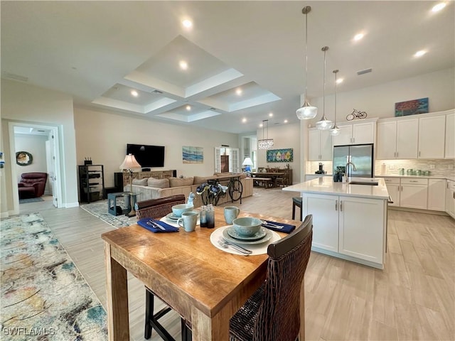 dining area with beamed ceiling, light wood-type flooring, sink, and coffered ceiling