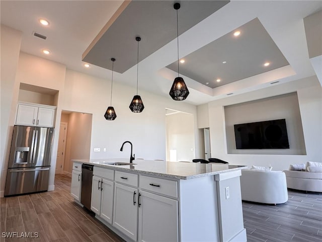 kitchen with appliances with stainless steel finishes, white cabinets, light stone counters, a tray ceiling, and a center island with sink