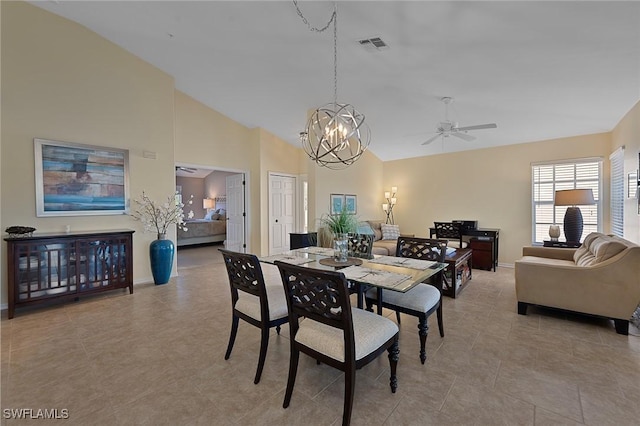 dining space with ceiling fan with notable chandelier, light tile patterned flooring, and high vaulted ceiling