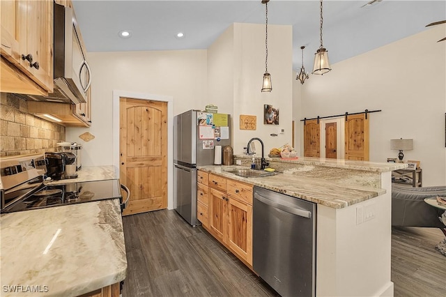 kitchen with light stone countertops, hanging light fixtures, a barn door, dark hardwood / wood-style floors, and appliances with stainless steel finishes