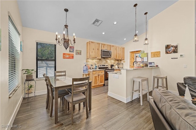 dining area featuring light hardwood / wood-style flooring, vaulted ceiling, a notable chandelier, and sink