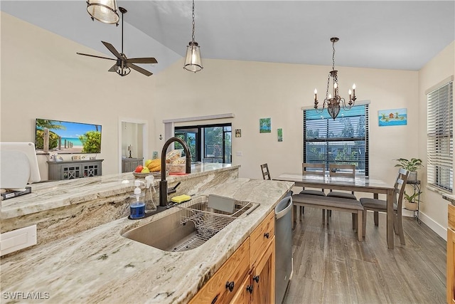 kitchen with light wood-type flooring, stainless steel dishwasher, ceiling fan with notable chandelier, sink, and pendant lighting