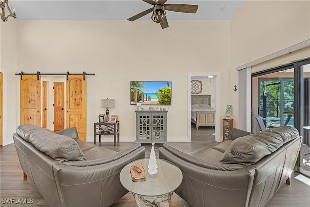 living room with hardwood / wood-style flooring, ceiling fan, a barn door, and a high ceiling