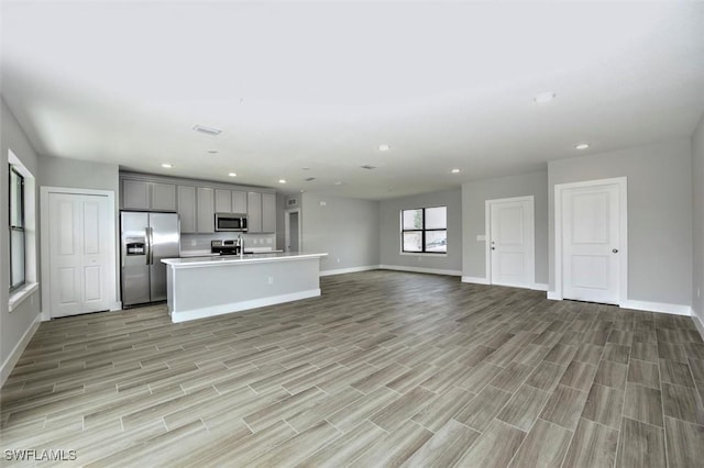 kitchen featuring gray cabinetry, an island with sink, stainless steel appliances, and light wood-type flooring