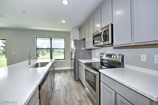 kitchen with gray cabinetry, sink, light wood-type flooring, and stainless steel appliances