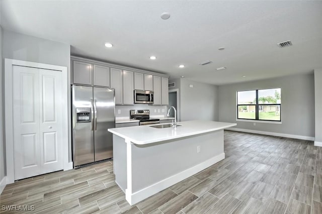 kitchen with gray cabinetry, a kitchen island with sink, sink, appliances with stainless steel finishes, and light hardwood / wood-style floors