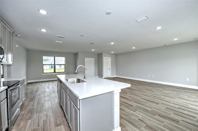 kitchen featuring sink, gray cabinets, an island with sink, appliances with stainless steel finishes, and light hardwood / wood-style floors