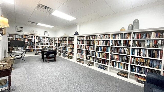 living area featuring wall of books, carpet floors, visible vents, and a drop ceiling