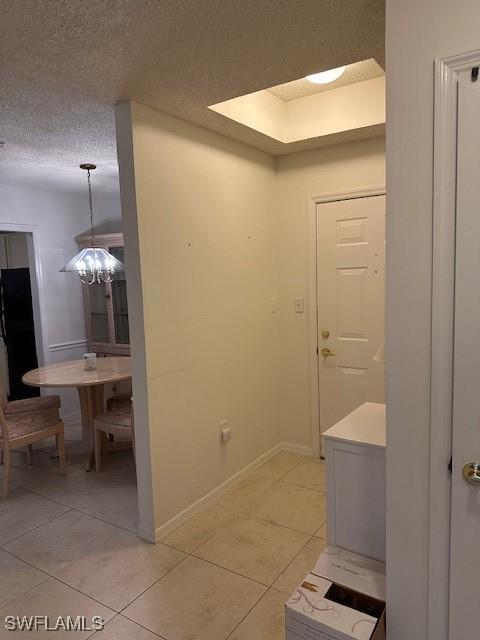 corridor featuring light tile patterned floors, a chandelier, and a textured ceiling