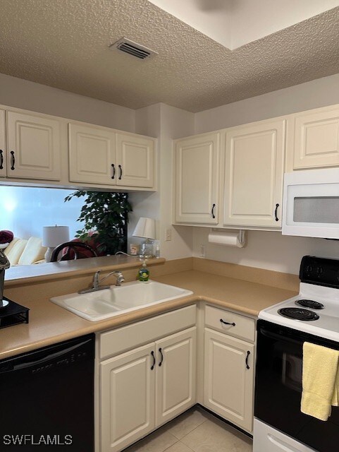 kitchen with a textured ceiling, white cabinetry, sink, and white appliances