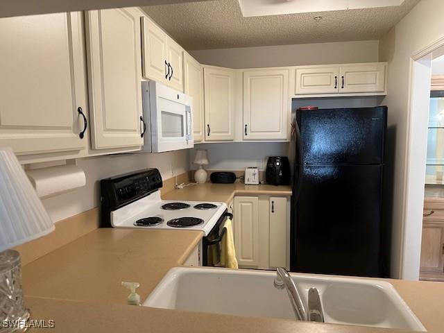 kitchen with electric stove, white microwave, freestanding refrigerator, light countertops, and a sink