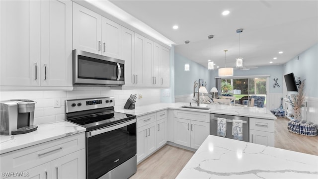 kitchen featuring white cabinetry, light stone counters, light hardwood / wood-style flooring, pendant lighting, and appliances with stainless steel finishes