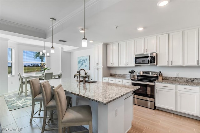 kitchen with sink, hanging light fixtures, stainless steel appliances, a center island with sink, and white cabinets